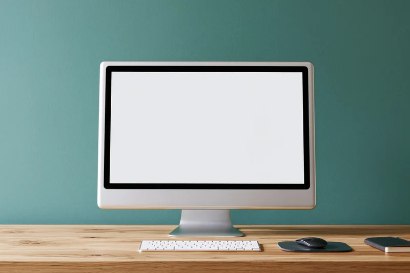 All-in-one computer with blank white screen on wooden desk against teal wall