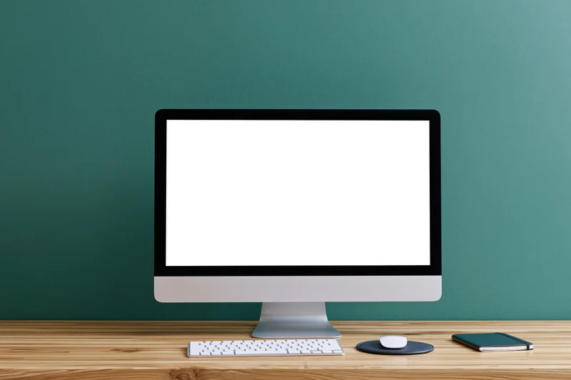 All-in-one computer with blank white screen on wooden desk against teal wall