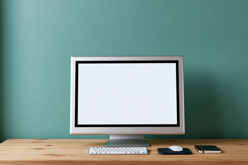 All-in-one computer with blank white screen on wooden desk against teal wall