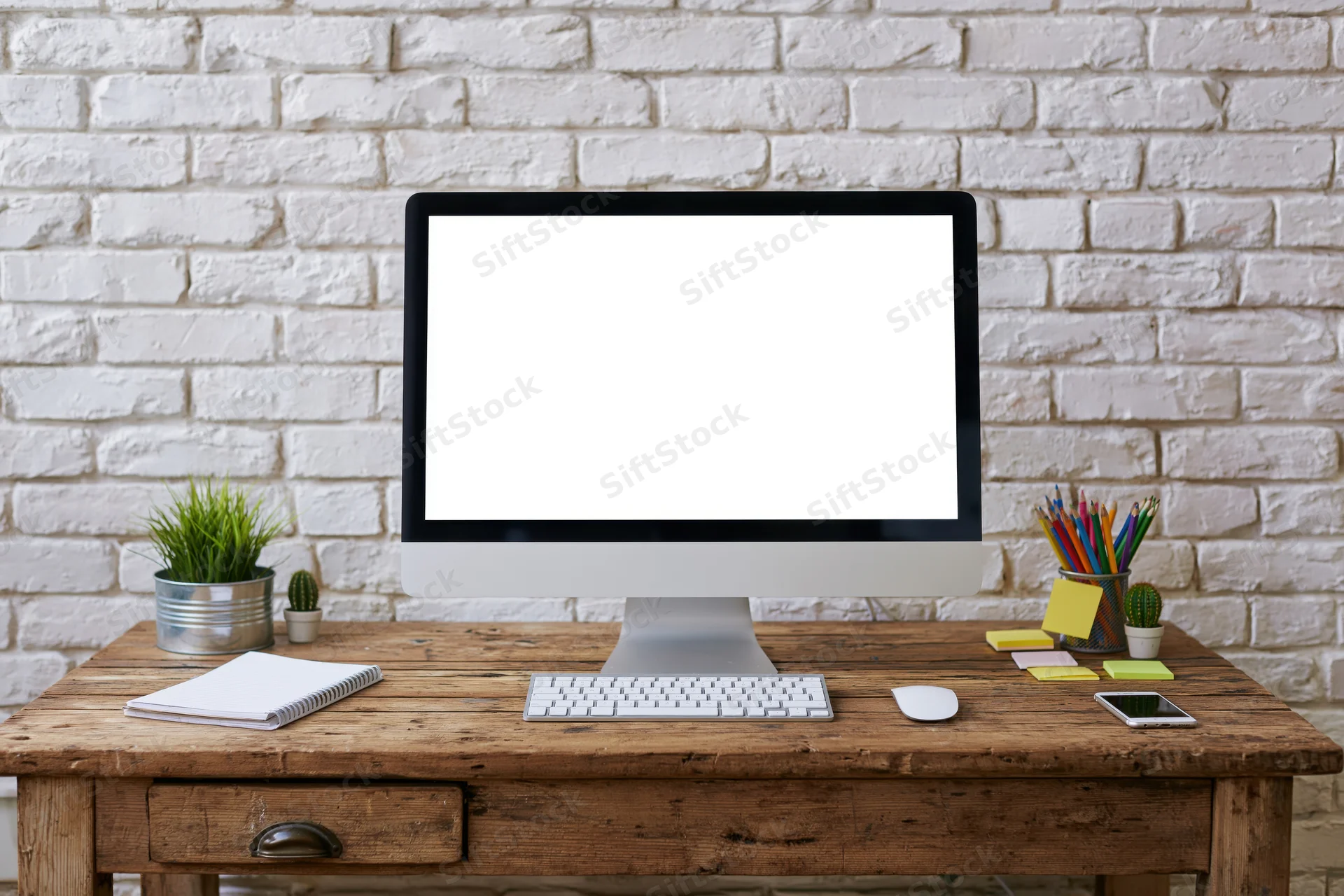 Computer monitor with blank screen on wooden desk against white brick wall