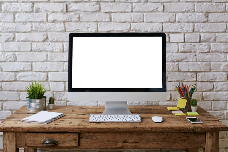 Computer monitor with blank screen on wooden desk against white brick wall