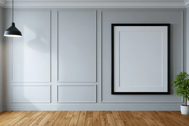 Empty black framed poster on light grey paneled wall with wooden floor and hanging lamp