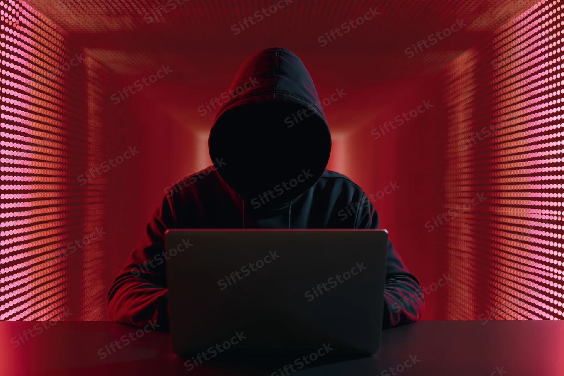 Hooded figure working on laptop in red-lit digital environment