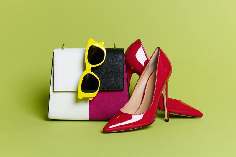 Red patent heels, yellow sunglasses and color-block handbag arranged on lime green background