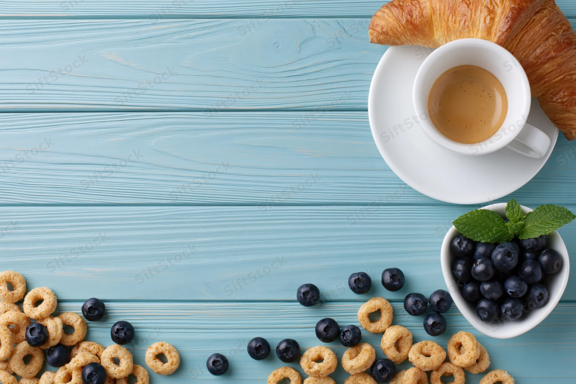 Breakfast spread with cereal, blueberries, croissant and coffee on a light blue wooden table
