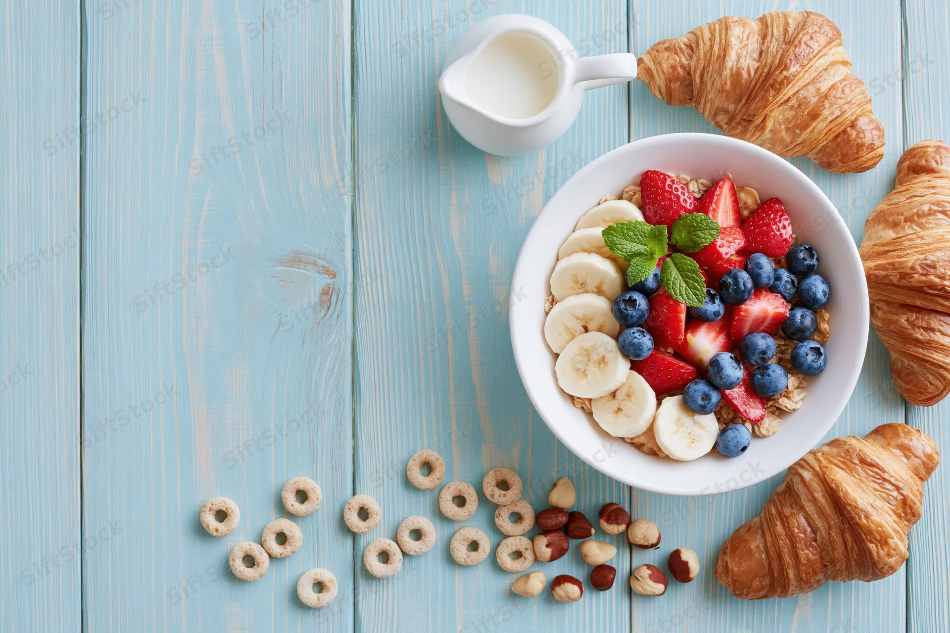 Breakfast spread with cereal, fruit, croissants and milk on a blue wooden table