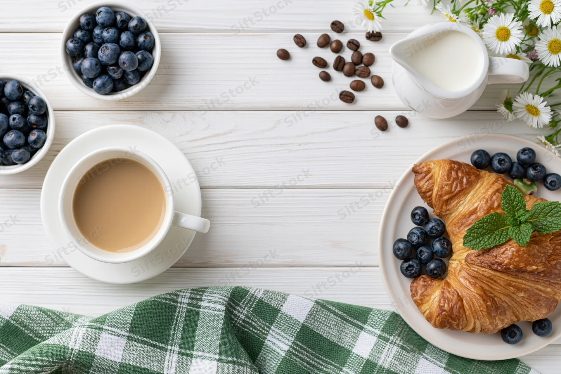 Breakfast spread with coffee, croissant, blueberries and milk on white wooden table