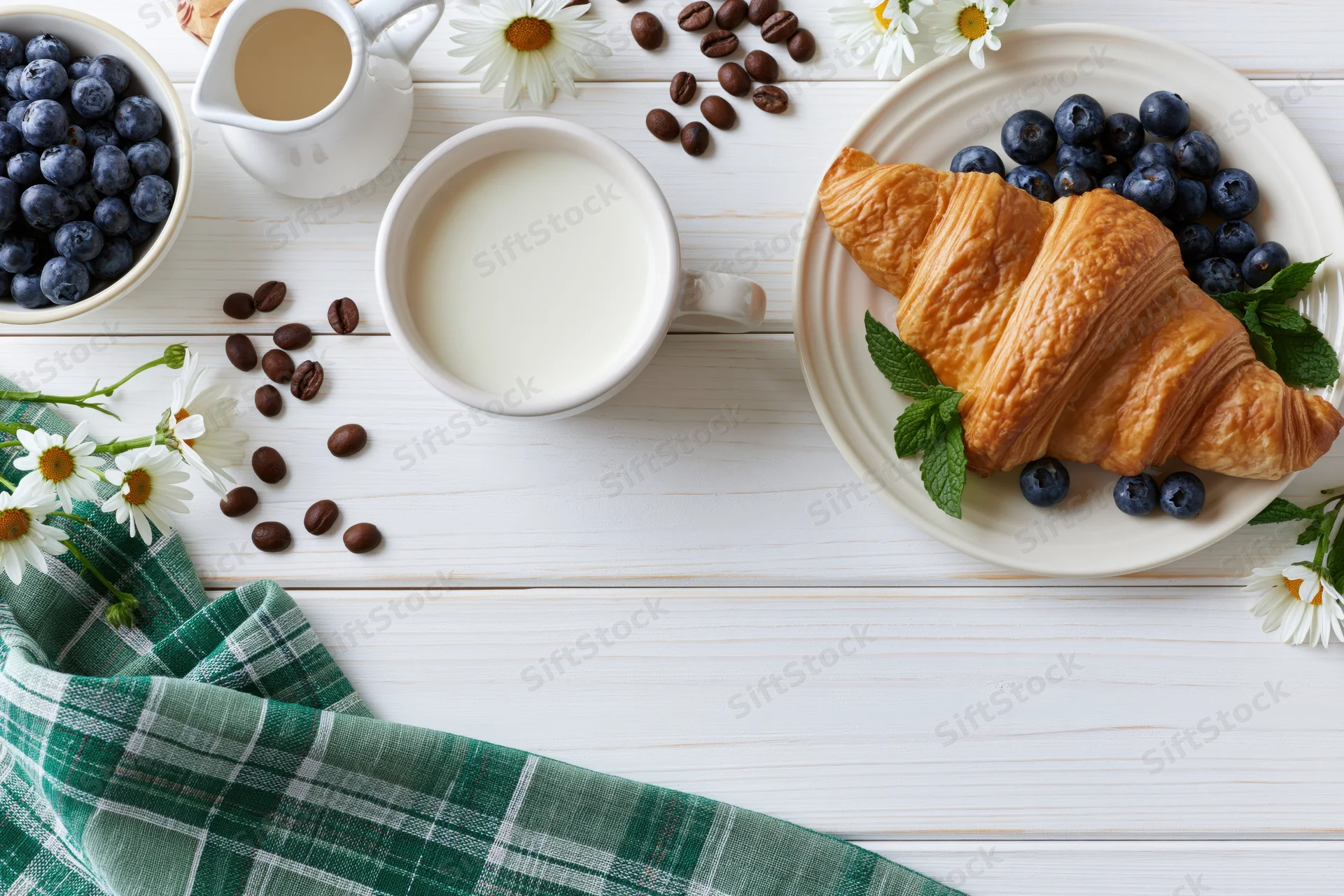 Flat lay breakfast spread with croissant, blueberries, coffee and milk on white wooden table