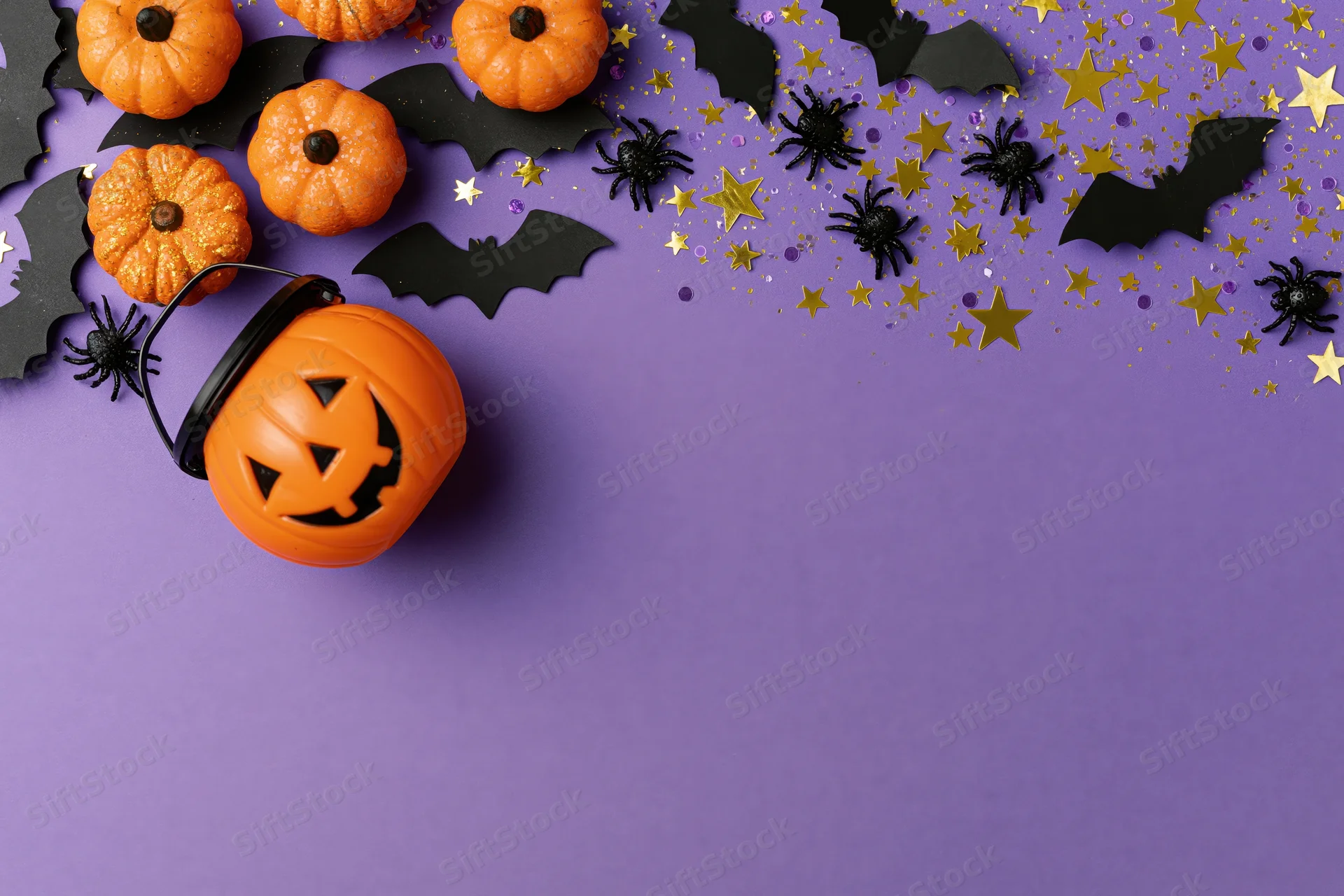 Halloween decorations arranged in flat lay on purple surface with copyspace