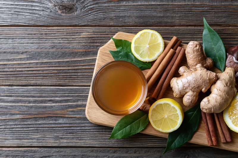 Glass cup of tea with ginger, lemon, cinnamon and leaves on wooden cutting board