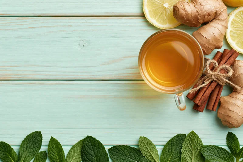Glass cup of herbal tea with ginger, lemon, mint and cinnamon on turquoise wooden table, flat lay with copyspace
