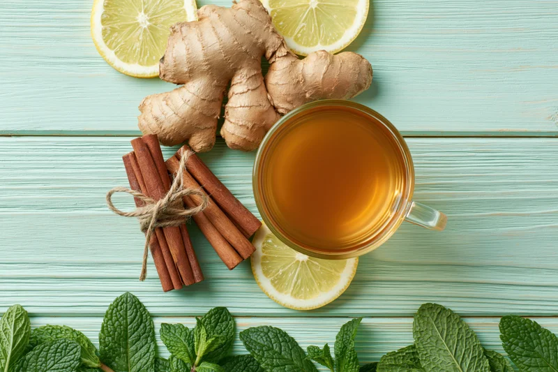 Glass cup of tea with ginger, lemon, mint and cinnamon sticks arranged on a light blue wooden surface