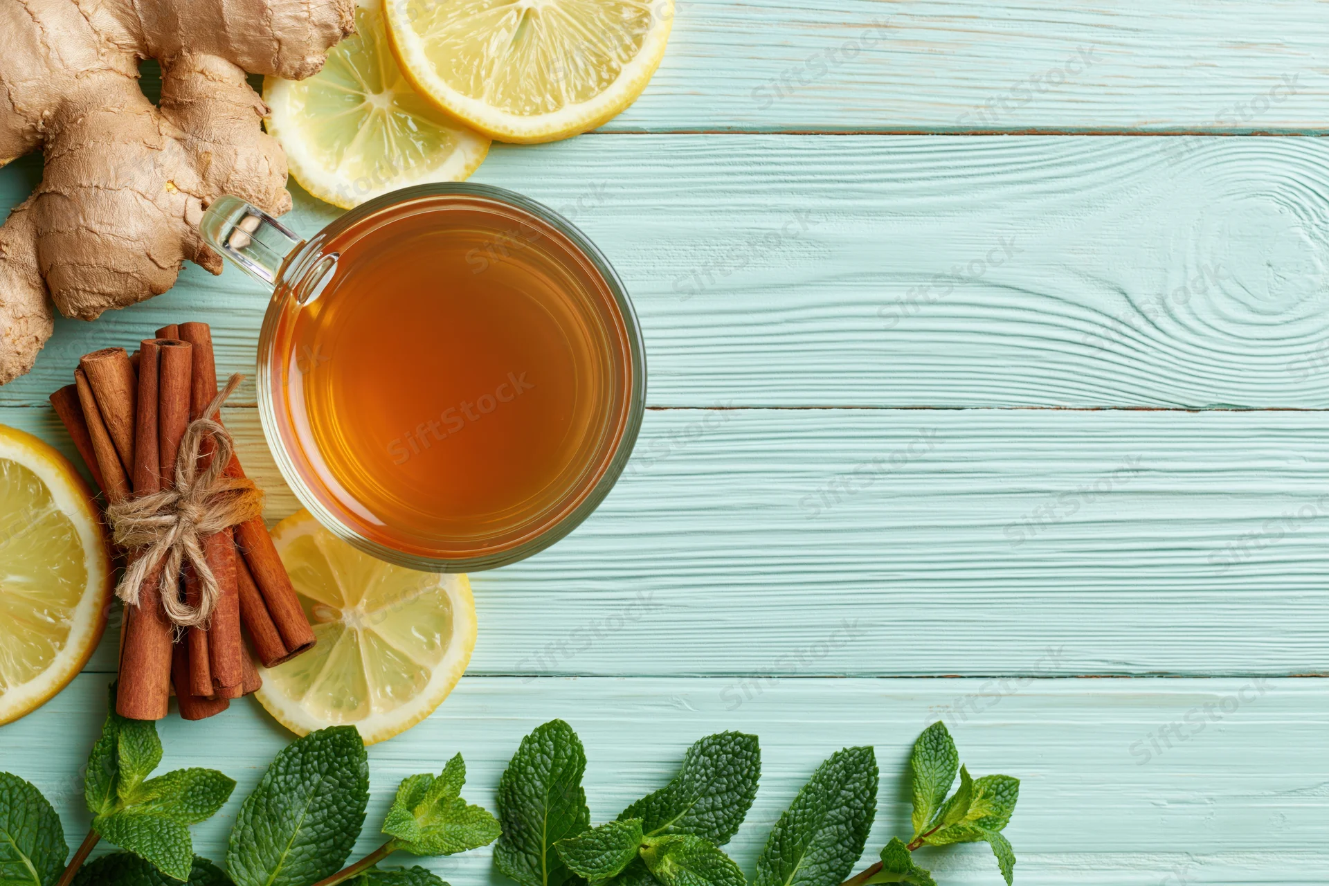Glass cup of tea with ginger, lemon, cinnamon and mint on a light blue wooden table, flat lay overhead view