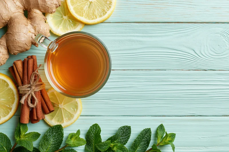 Glass cup of tea with ginger, lemon, cinnamon and mint on a light blue wooden table, flat lay overhead view