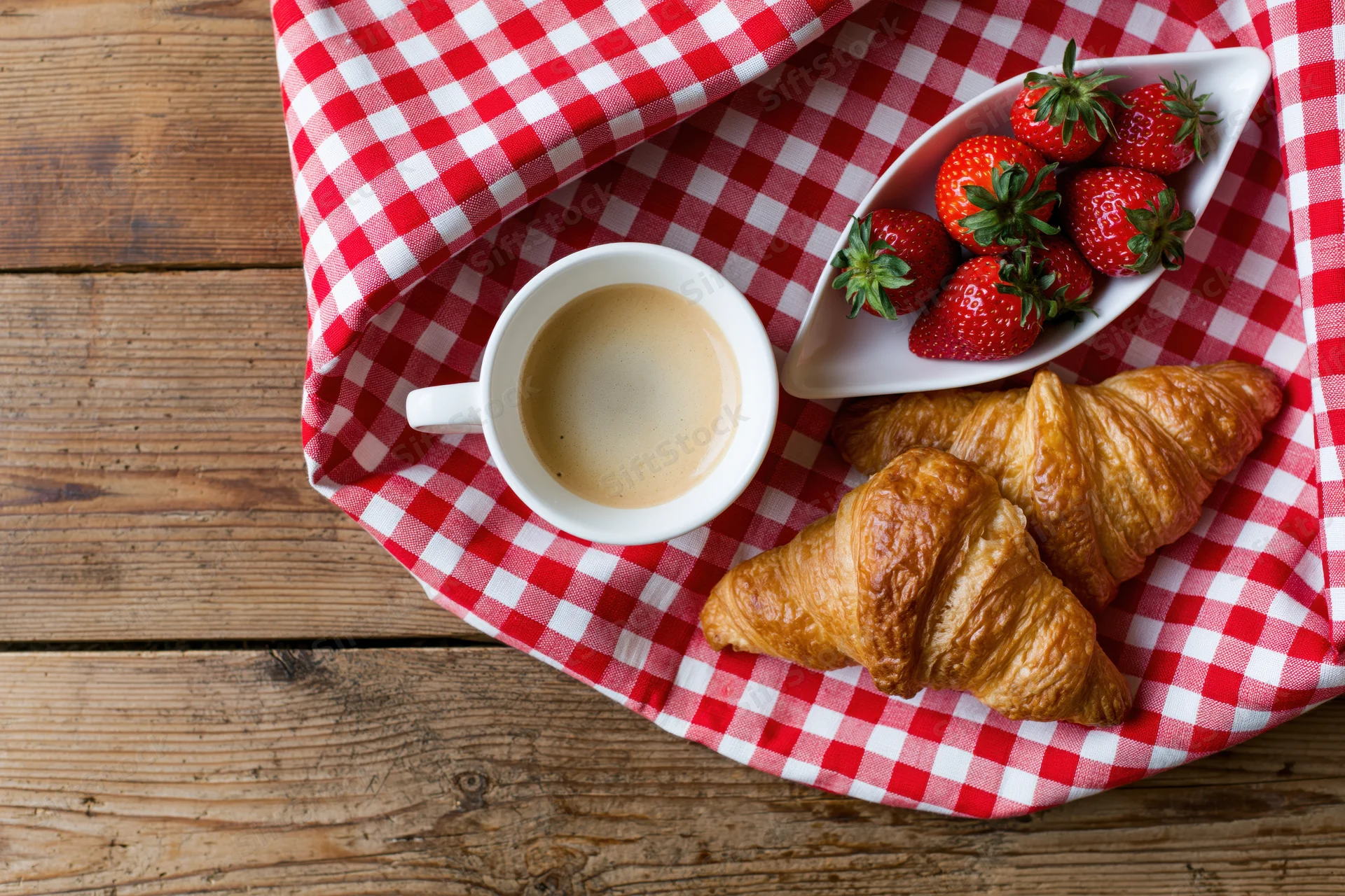 Croissants and coffee with strawberries on a checkered napkin on wooden table