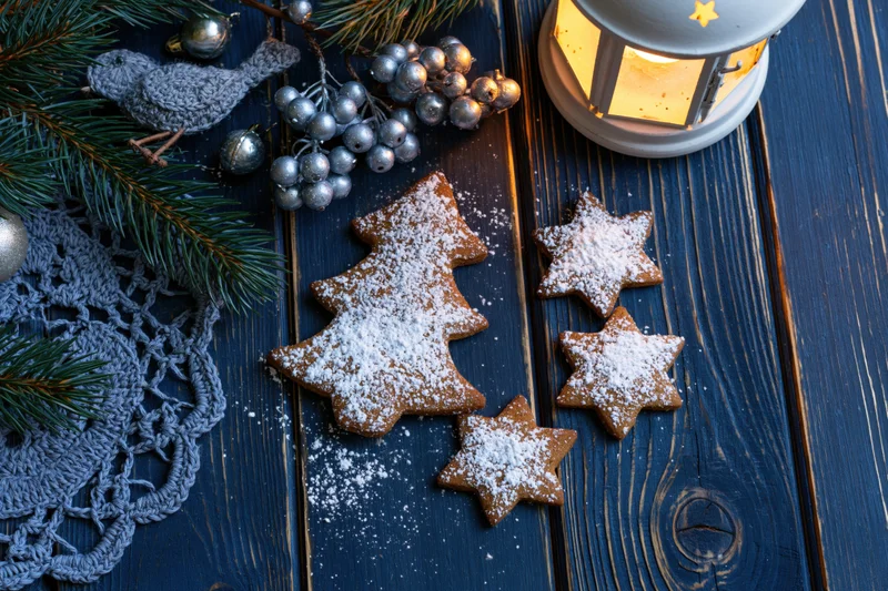 Gingerbread cookies shaped as christmas tree and stars dusted with powdered sugar on dark wooden table with pine branches and silver ornaments