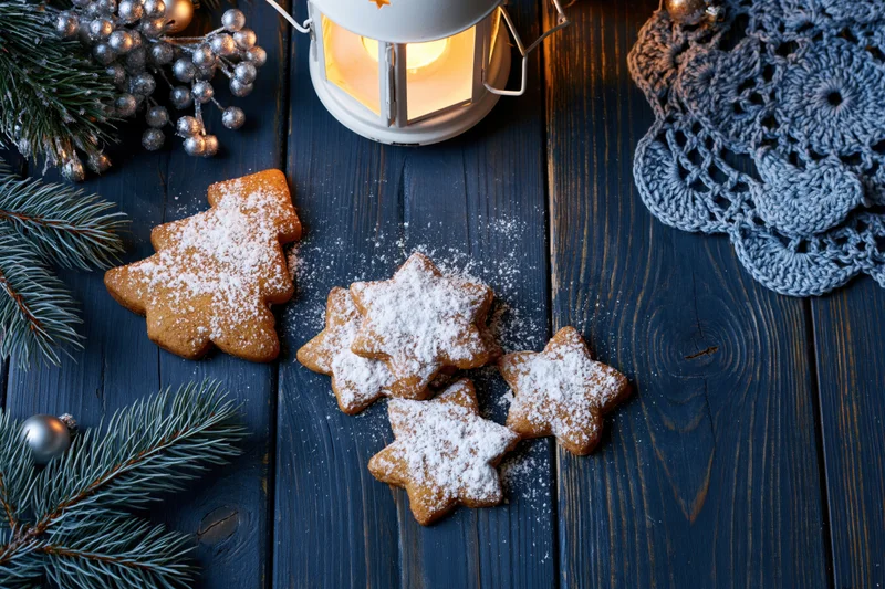 Gingerbread cookies shaped as christmas tree and stars on dark wooden table with pine branches and lantern