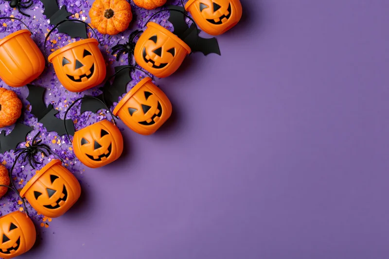 Orange plastic jack-o-lantern candy buckets arranged in a flat lay on purple surface with bats and glitter for halloween decoration