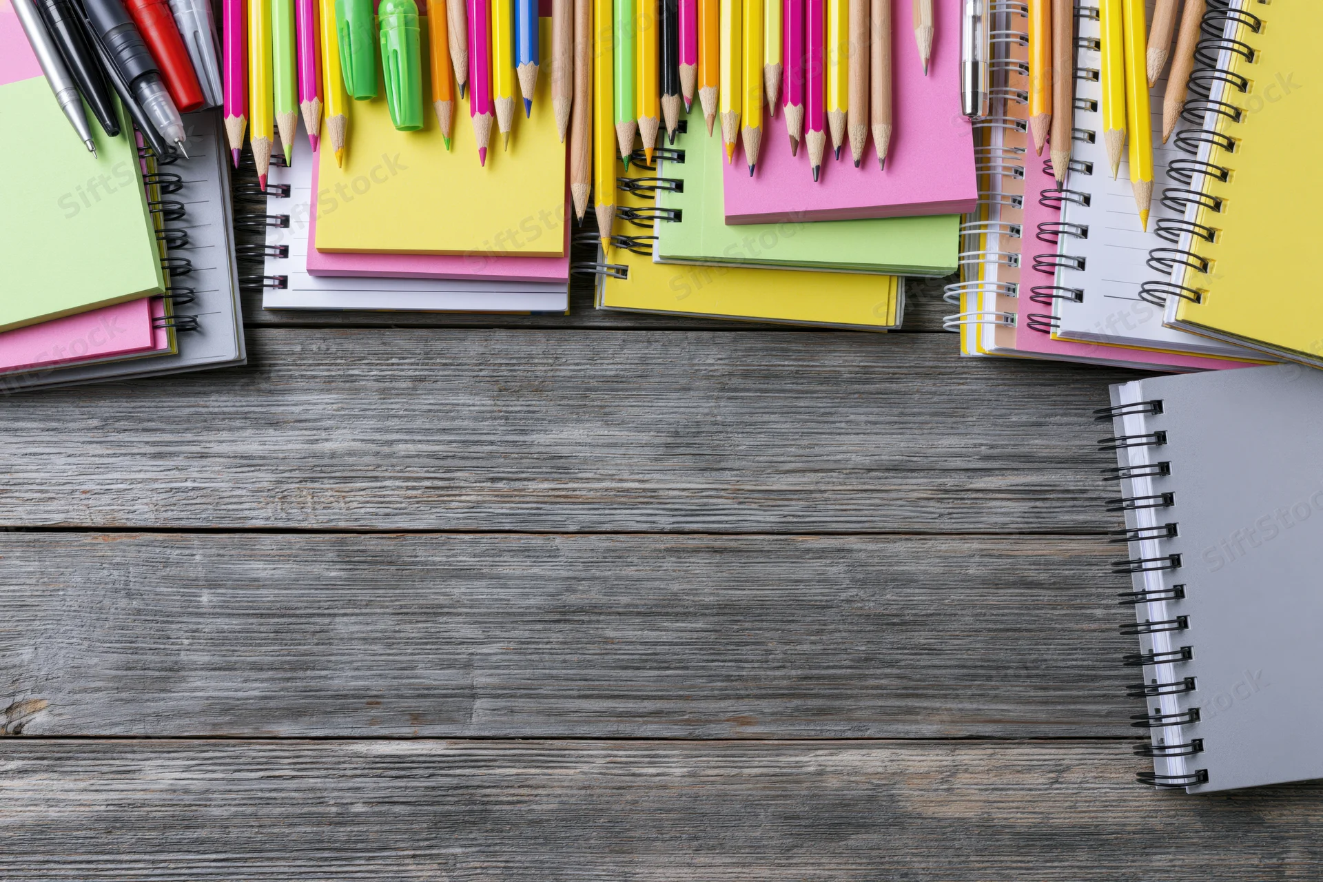 Colorful stationery and notebooks arranged on wooden surface with copyspace