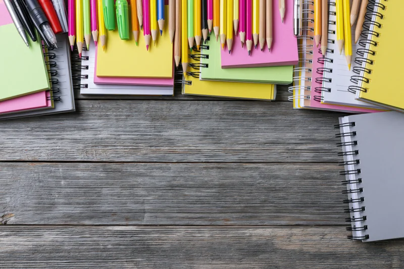 Colorful stationery and notebooks arranged on wooden surface with copyspace