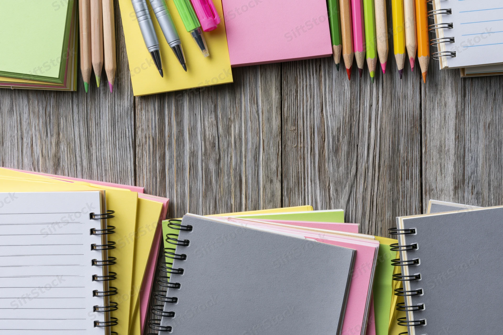 Spiral notebooks and colorful sticky notes arranged on a wooden surface with pencils and pens for study or office use