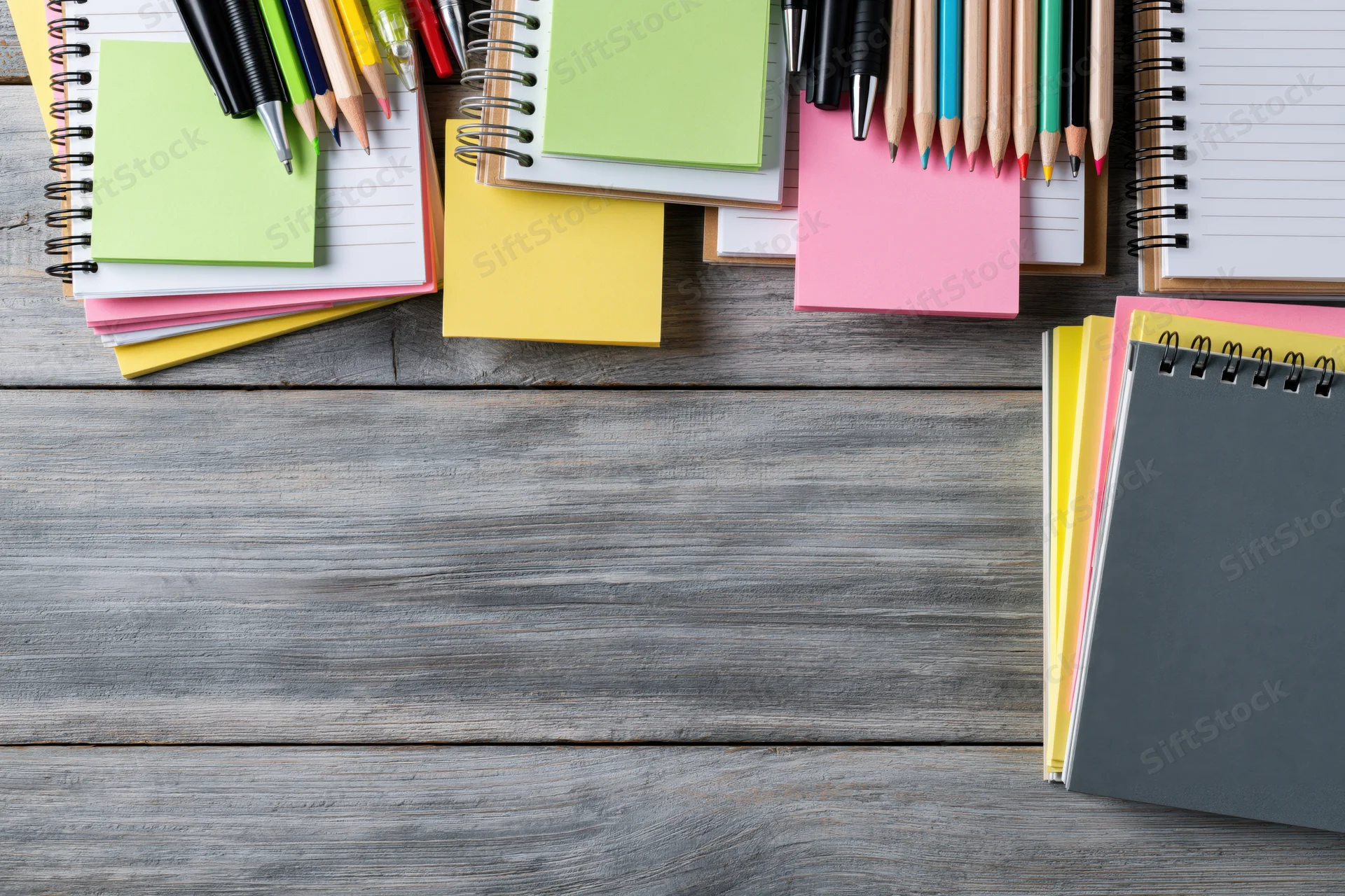 Spiral notebooks and colorful sticky notes arranged on a wooden desk with copyspace below