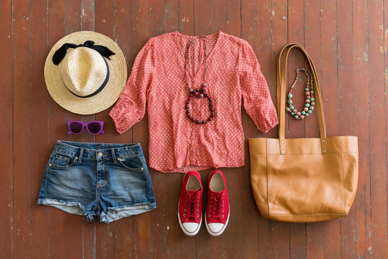 Women's summer outfit with accessories arranged flat on wooden floor