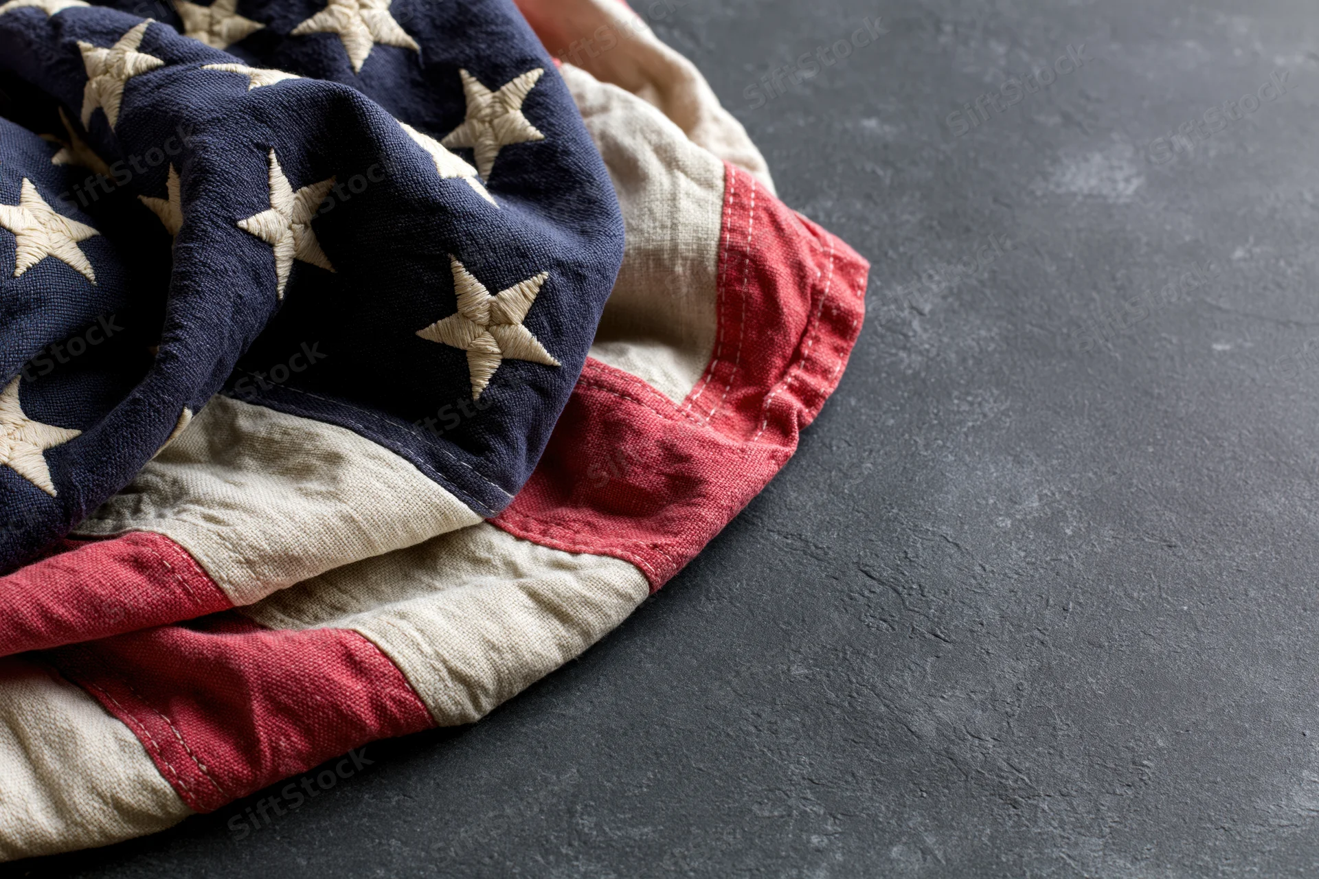 Folded american flag with stars and stripes resting on dark textured surface