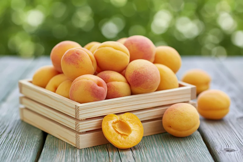 Fresh apricots piled in a wooden crate on a weathered outdoor table