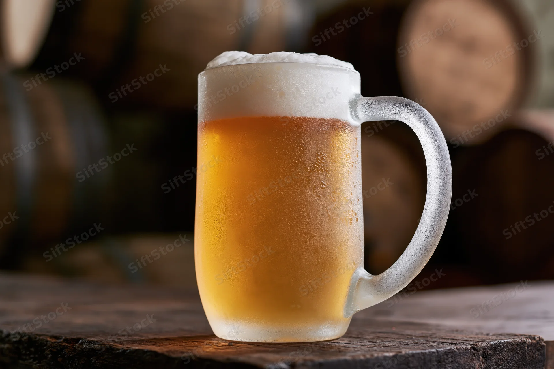 Frosted glass beer mug filled with pale lager and thick foam on wooden table with barrels in background