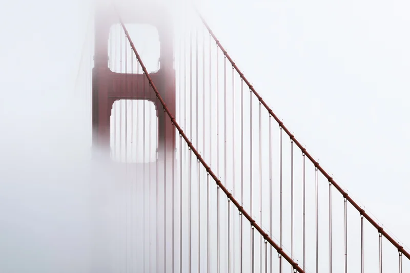 Golden gate bridge tower emerging from dense fog with cables stretching diagonally across frame