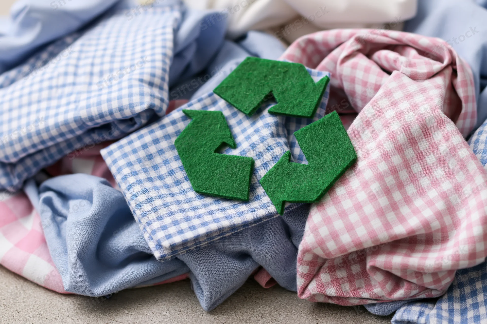 Green felt recycling symbol on a pile of checkered and solid cotton clothing