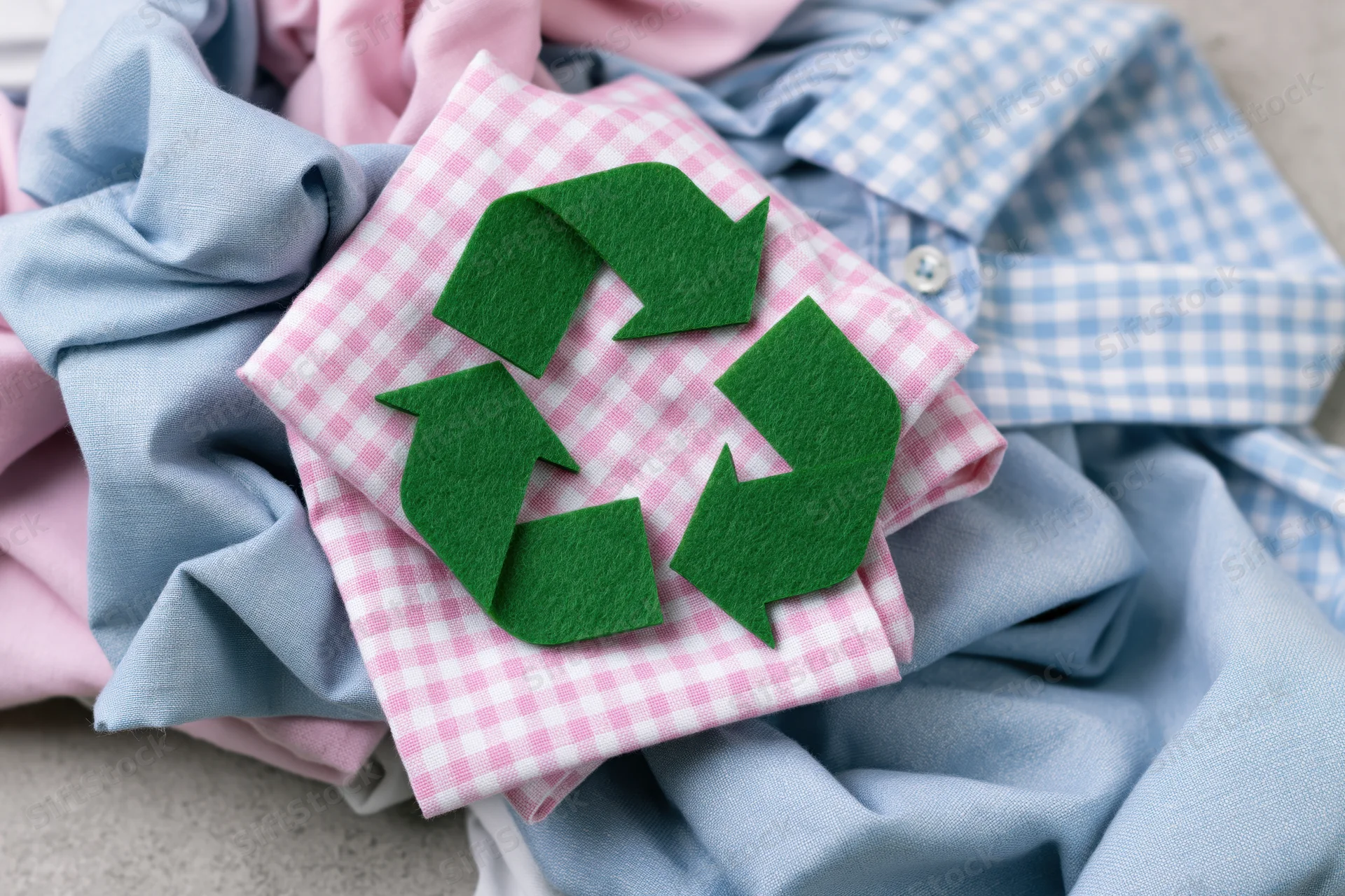 Green felt recycling symbol on a pile of folded clothes in pink and blue patterns