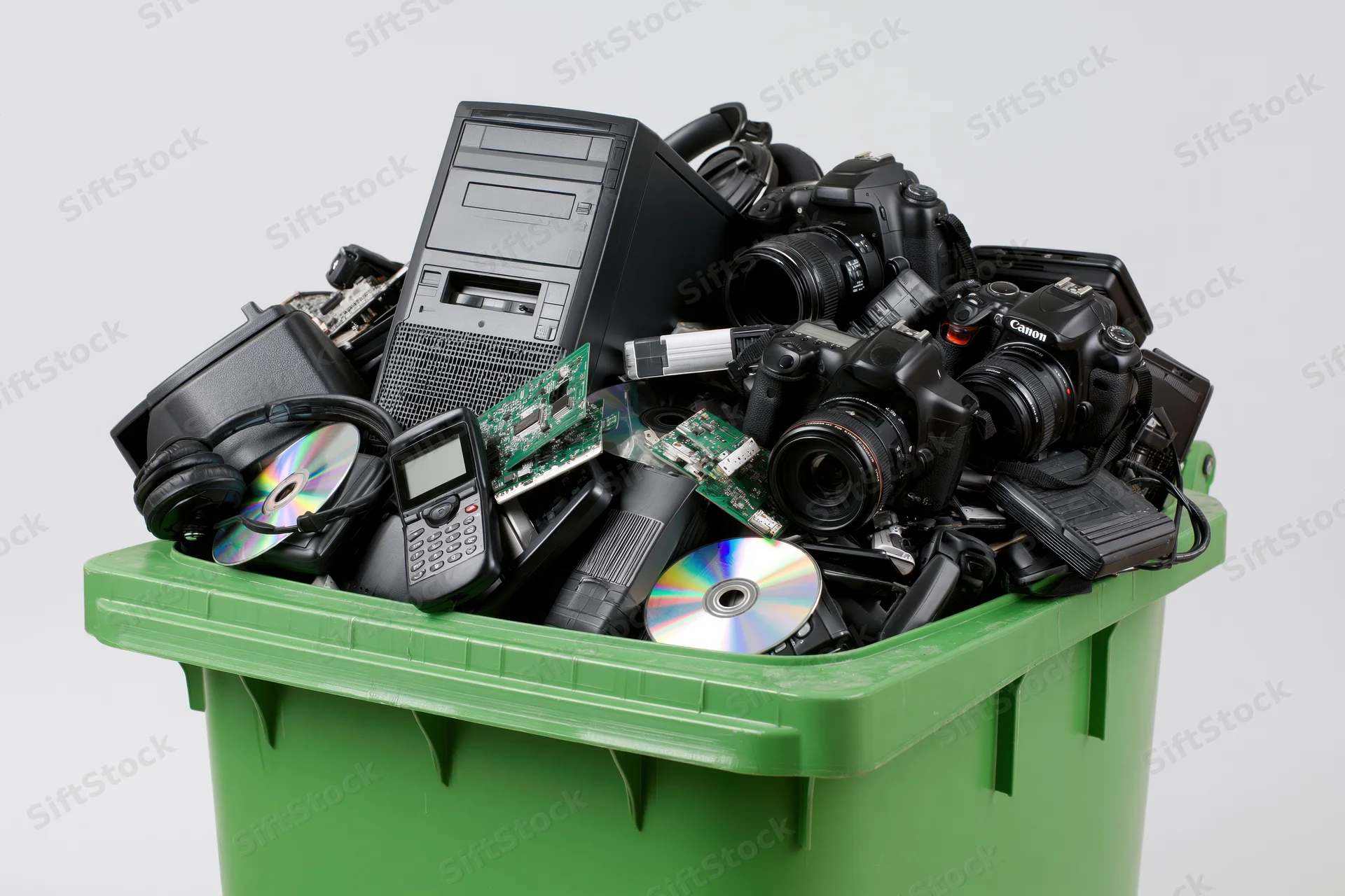 Green plastic bin overflowing with discarded electronics and digital devices