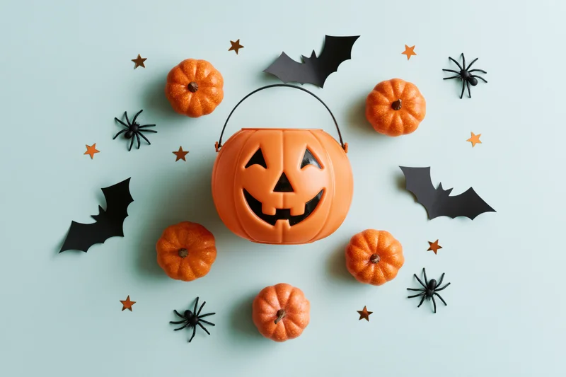 Smiling jack-o-lantern candy bucket surrounded by small pumpkins, bats, spiders and stars on a mint background