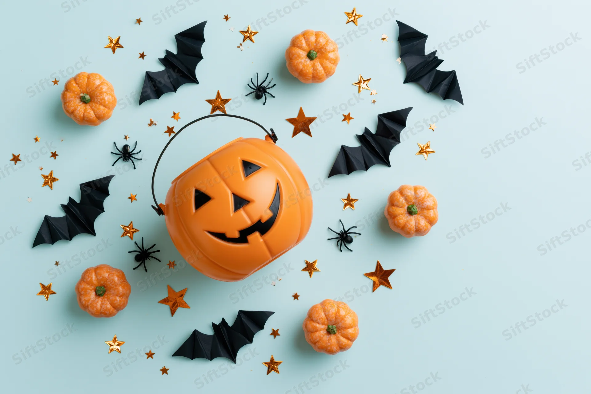 Smiling jack-o-lantern candy bucket surrounded by pumpkins, bats, spiders and stars on light blue background