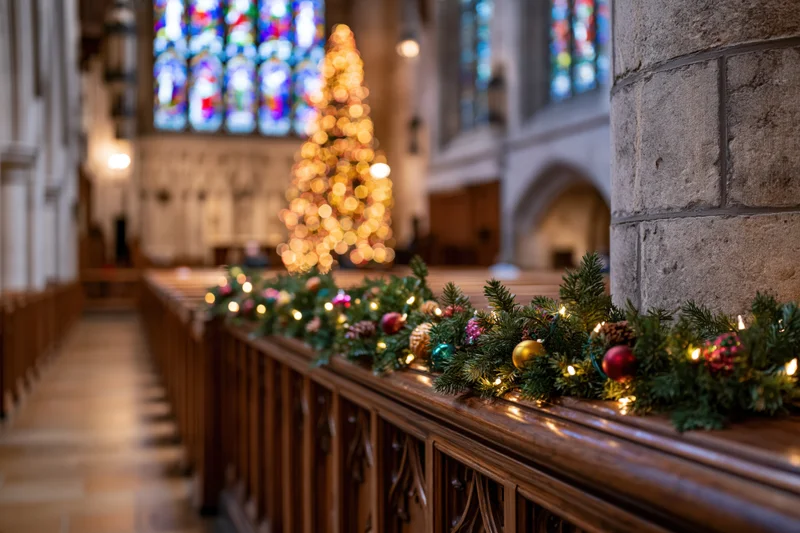 Christmas garland with lights and ornaments adorning wooden pews inside a gothic stone church