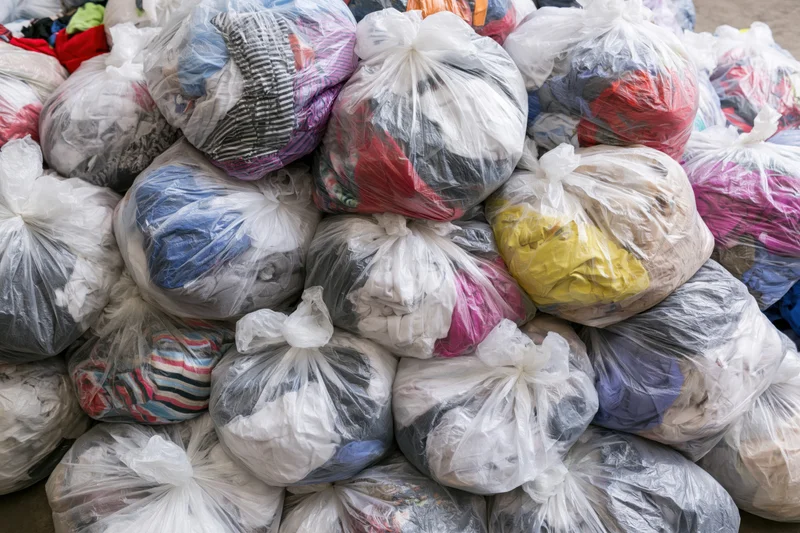 Large pile of clear plastic bags filled with mixed clothing and textiles for donation or recycling