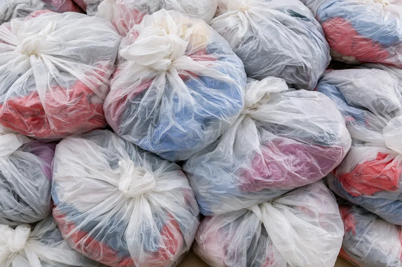 Pile of clear plastic bags filled with secondhand clothing, tied and stacked for donation