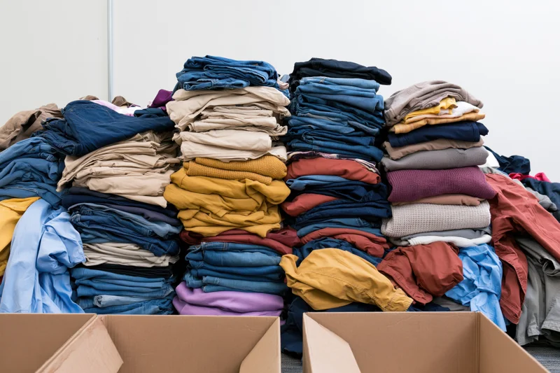 Large pile of folded donated clothing stacked in a warehouse with cardboard boxes in foreground