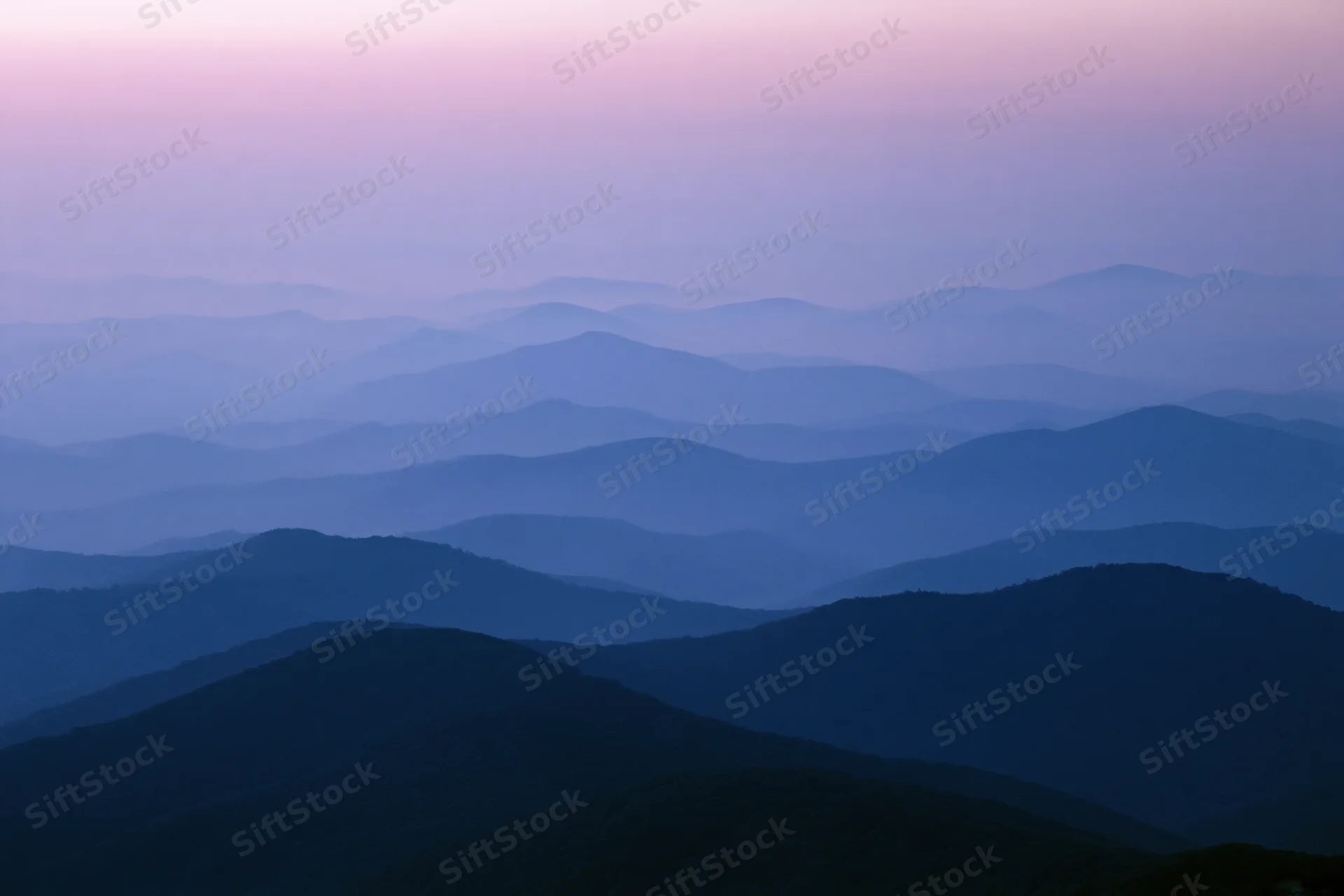 Layered mountain ridges receding into hazy distance at twilight