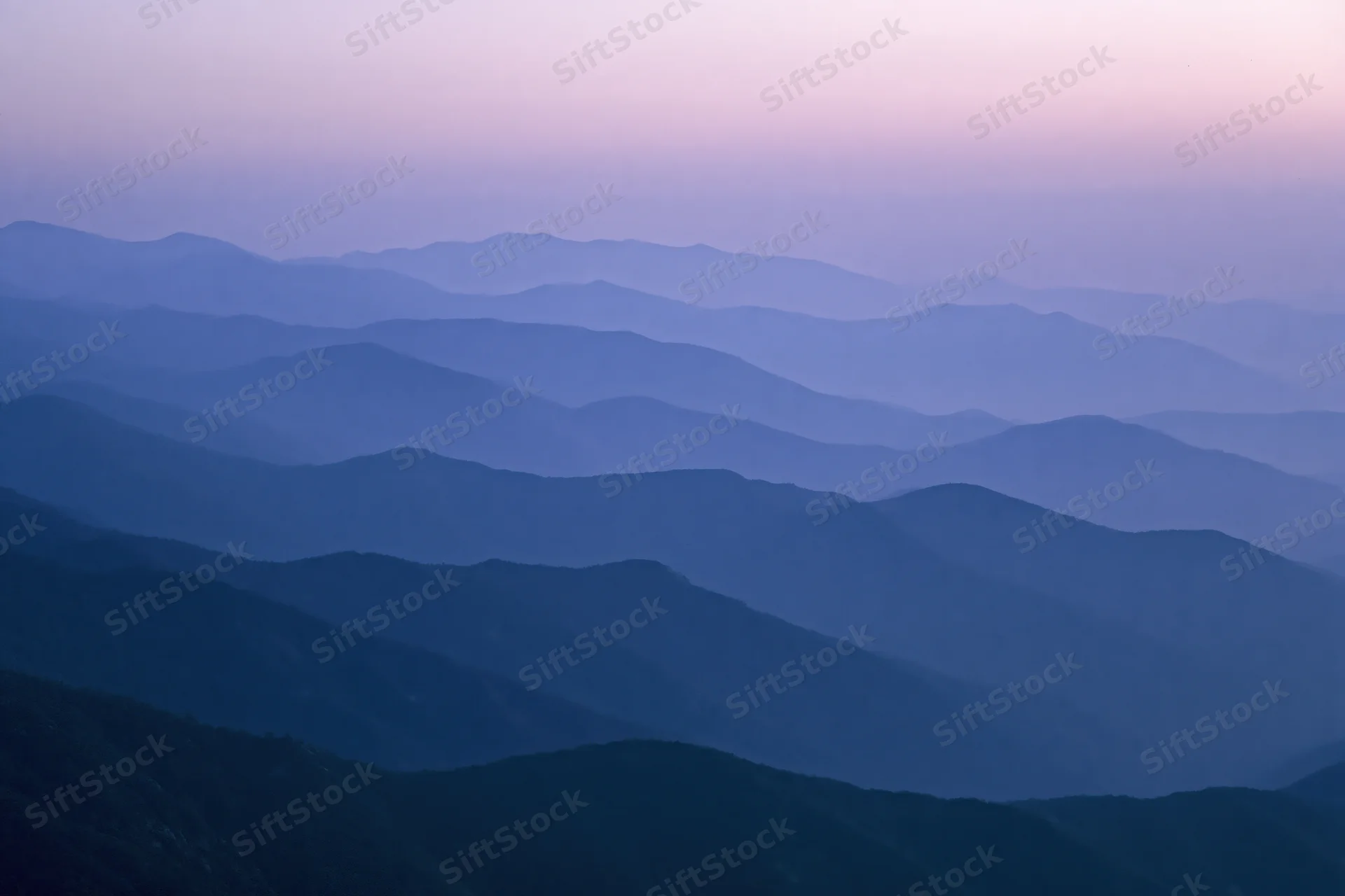 Layered mountain ridges receding into hazy distance at twilight