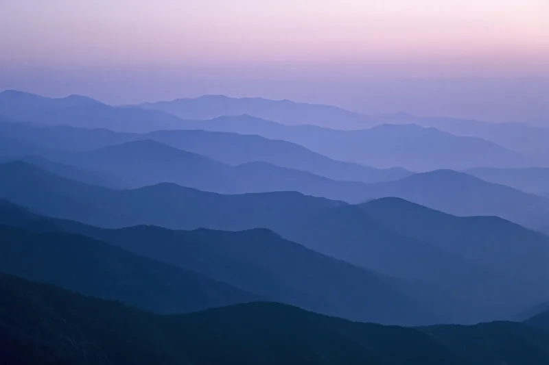 Layered mountain ridges receding into hazy distance at twilight