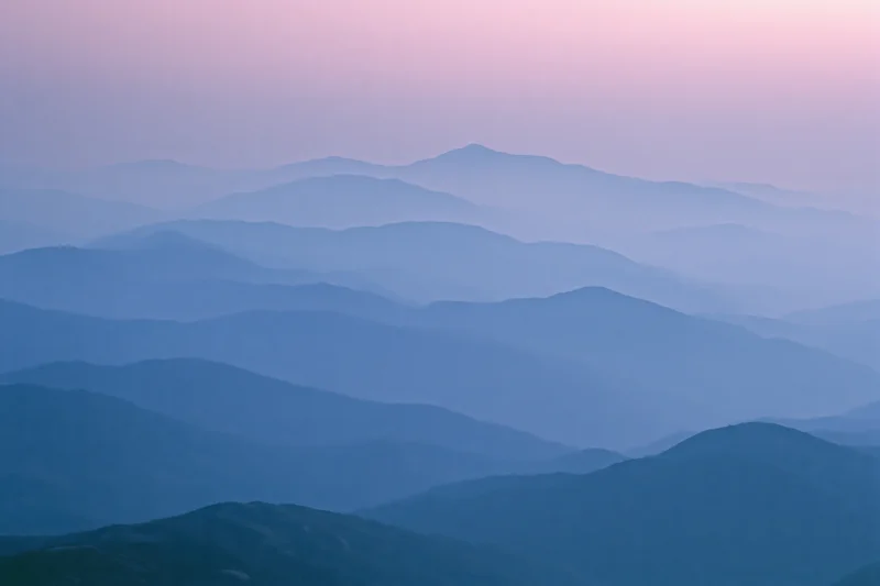 Layered mountain ridges receding into hazy distance at twilight
