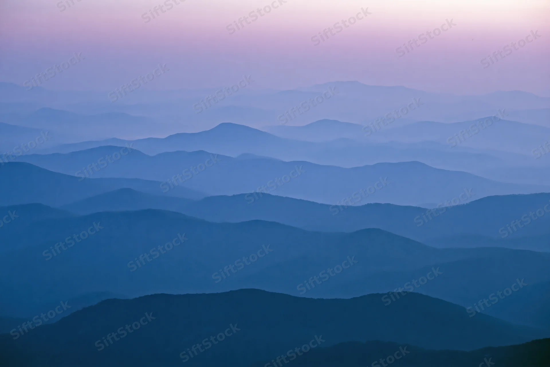 Layered mountain ridges receding into hazy distance at twilight