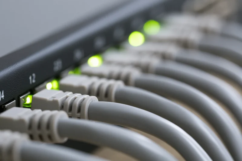 Gray ethernet cables plugged into a black network switch with green led indicators lit