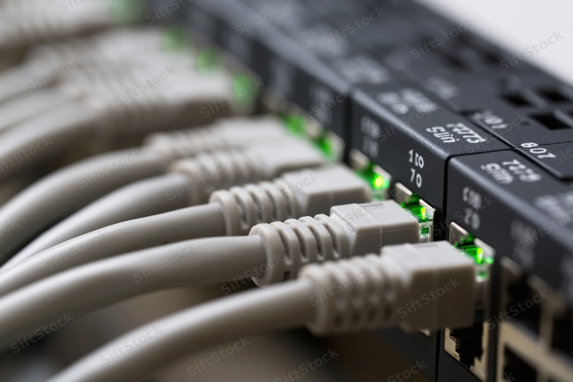 Gray ethernet cables plugged into a black network switch with green led indicators lit