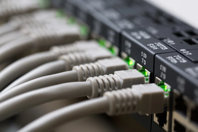 Gray ethernet cables plugged into a black network switch with green led indicators lit