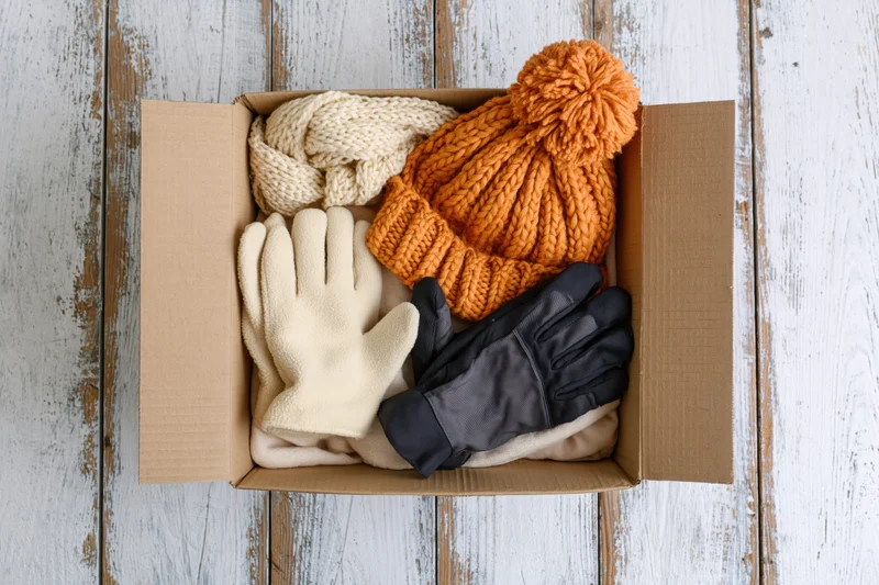 Open cardboard box filled with winter accessories on wooden surface