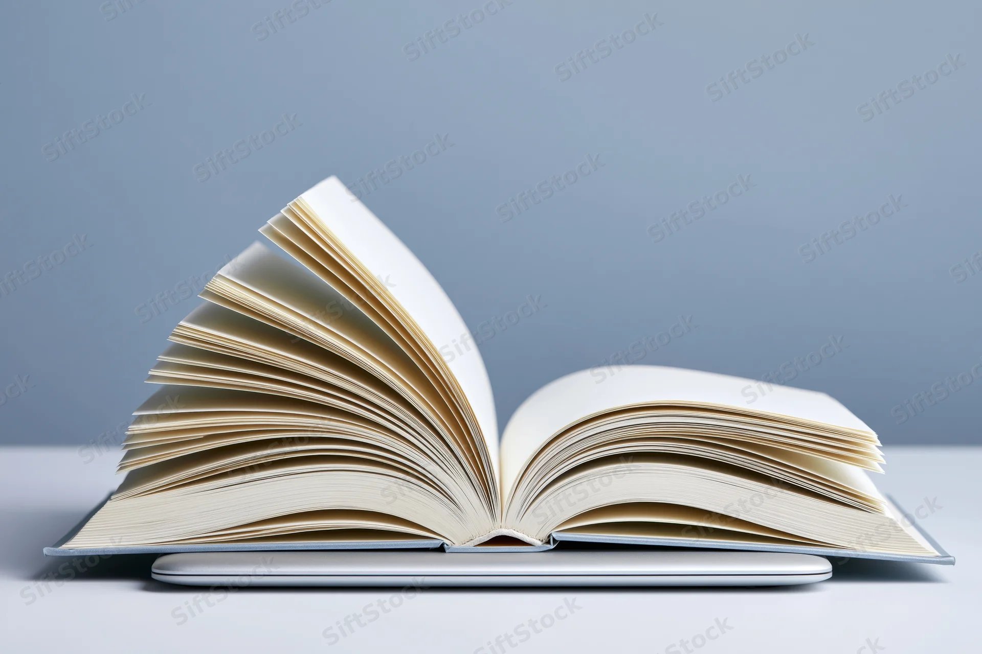 Open hardcover book with pages fanned outward resting on a closed laptop against a gray background